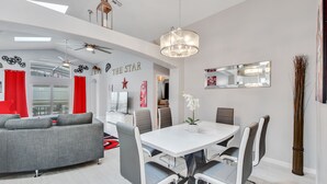 Un área de comedor moderna con una mesa blanca y sillas grises, un sofá gris y un ventilador de techo.