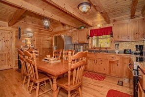 L’intérieur d’une cabane en bois comprend une table à manger entourée de chaises, un coin cuisine avec des placards en bois et un réfrigérateur.