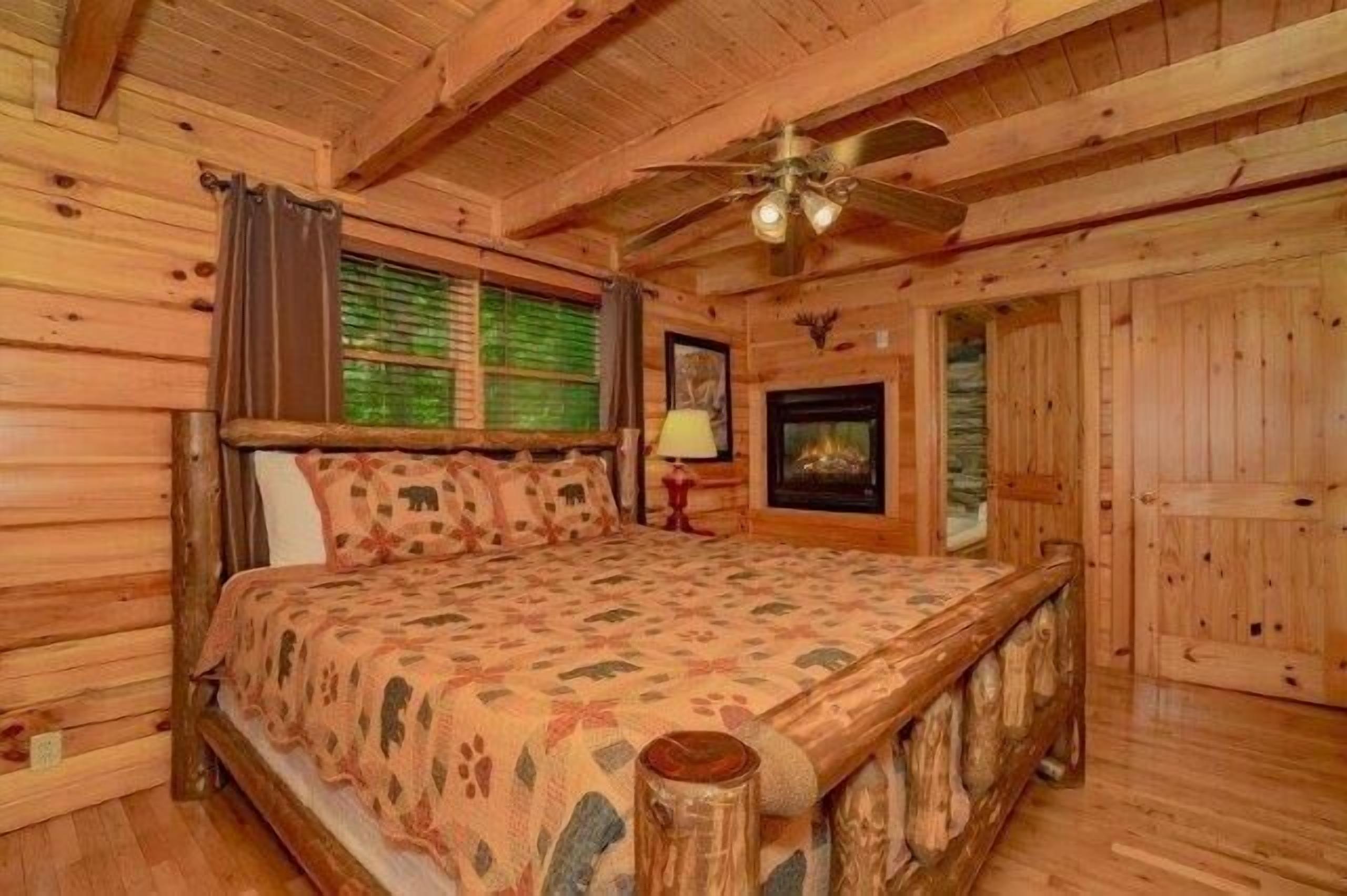 Een slaapkamer in blokhutstijl met een houten bed, een plafondventilator en een open haard.