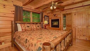Quarto em estilo cabana de tronco, com cama de madeira, ventilador de teto e lareira.