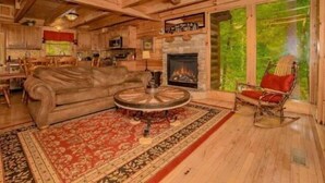Interior acolhedor de uma cabana de madeira com lareira, móveis rústicos e uma grande janela com vista para a vegetação.