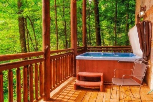 A wooden deck with a hot tub, two chairs, and a view of a dense forest.
