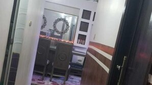 Un pasillo con alfombra floral, una puerta de madera oscura y un comedor con espejo y sillas.