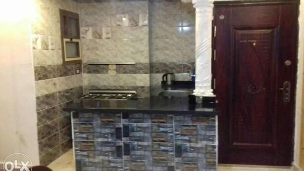 Una cocina con protector contra salpicaduras de piedra, encimera oscura y puerta de madera.