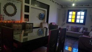 Una sala de estar con una mesa de centro de vidrio, varias sillas, un sofá y un ventanal con cortinas.