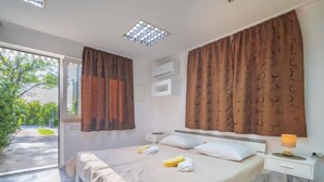 Un dormitorio con cama, mesita de noche con lámpara y vista a un jardín a través de una puerta de vidrio.