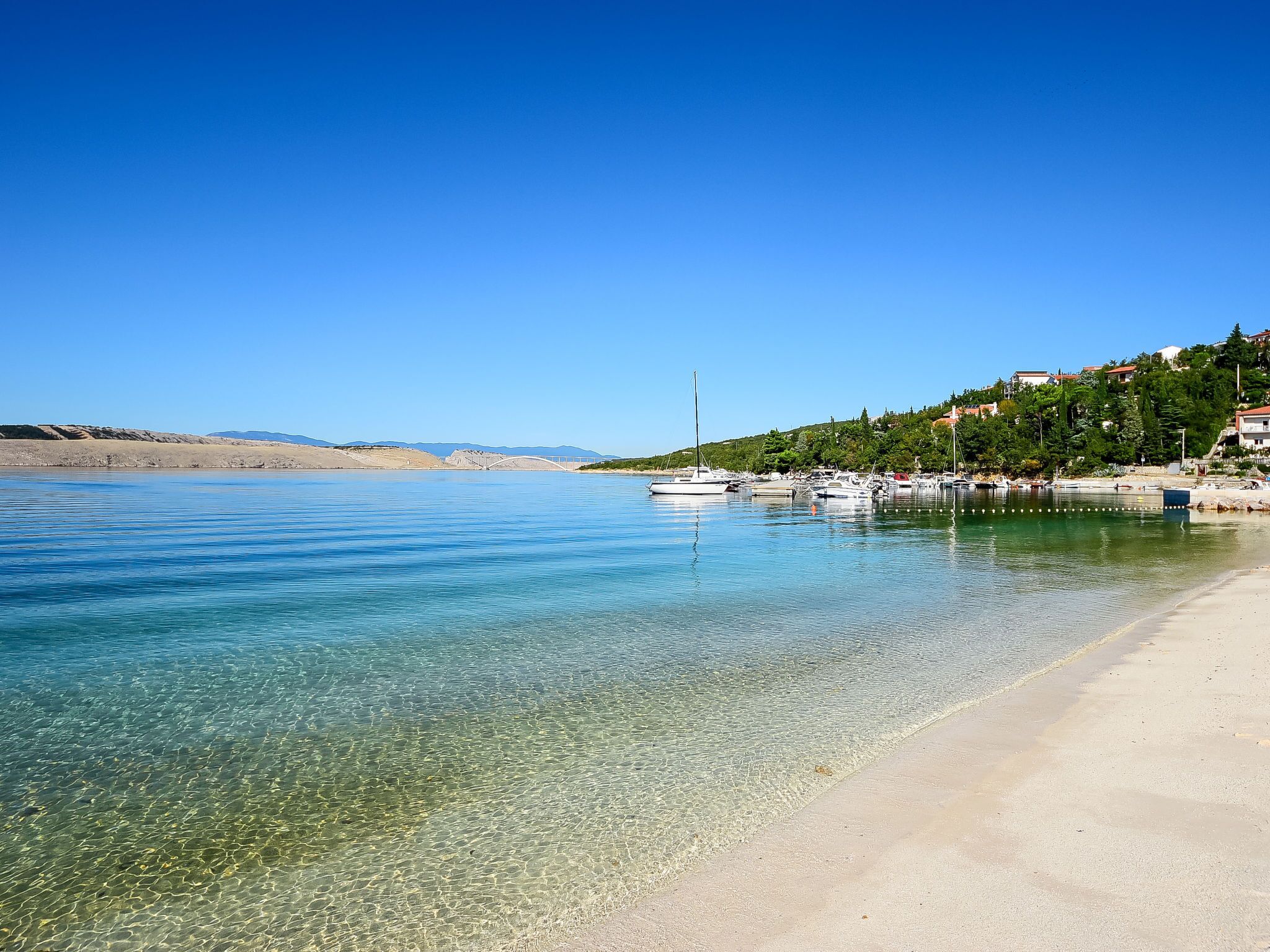 Une vue dégagée sur la côte, avec une plage de sable, une eau calme et un petit bateau amarré près du rivage.