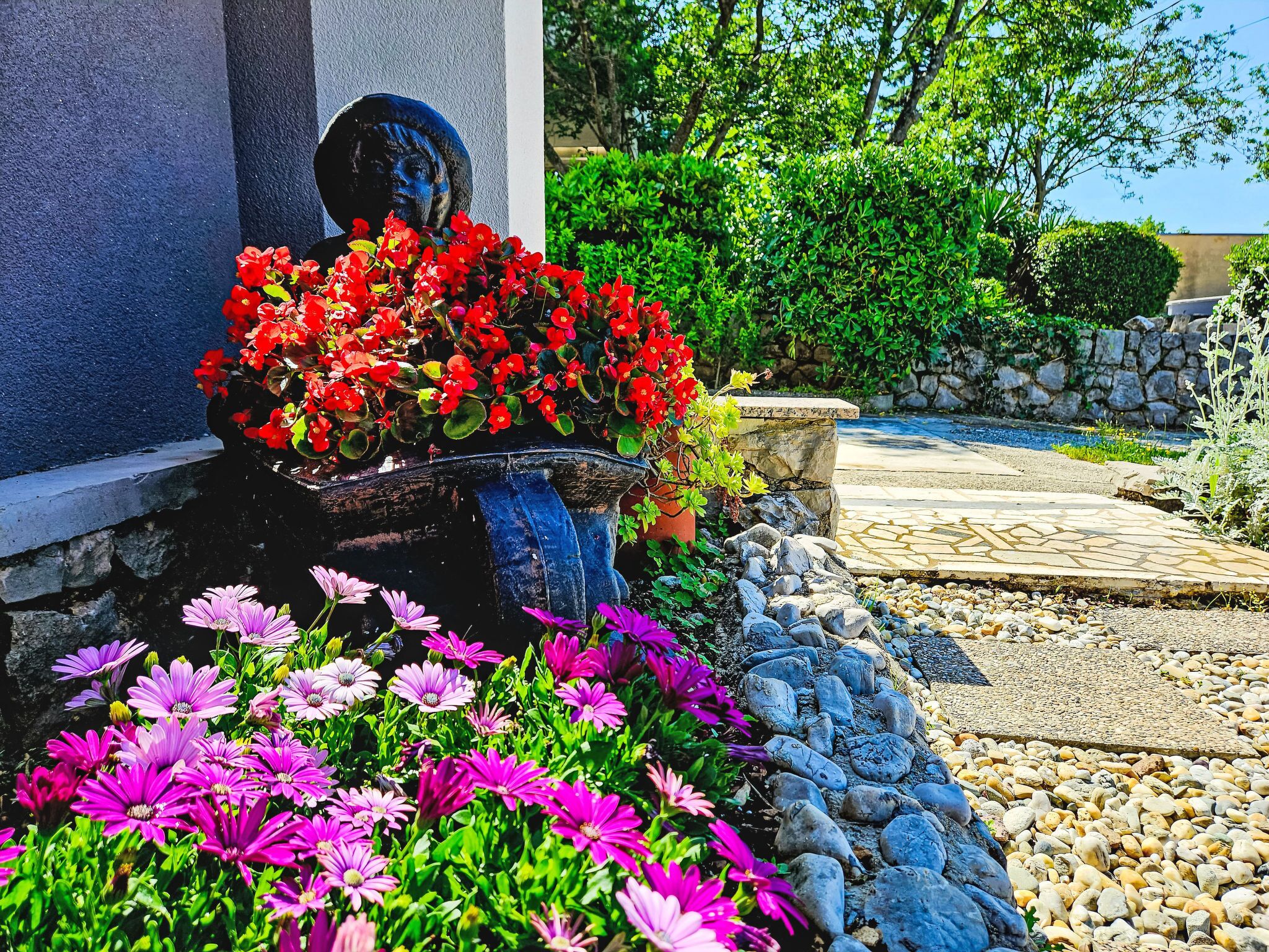 En have med en statue, farverige blomster og en stentrappe.