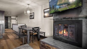 A modern living room with a fireplace, a dining area, and a mounted TV. - Modern Edelweiss 2 bedroom Condo! Fantastic views and some of the best ski access!! (Whitefish)