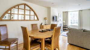Een eetgedeelte met een houten tafel en stoelen, een bank, en een groot rondboogvenster.
