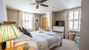 Een slaapkamer met een bed, een plafondventilator, een televisie en een raam met gordijnen.