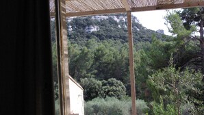 A view through a window with a wooden frame, overlooking a mountainous landscape with dense greenery and a building partially visible in the foreground.