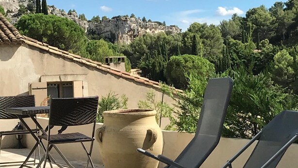 A rooftop terrace with lounge chairs, a large terracotta pot, and a view of rocky hills and trees.