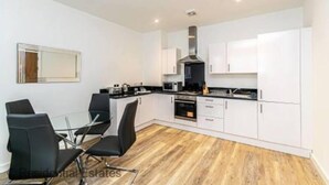 Una cocina moderna con armarios blancos, encimera negra y un comedor con sillas negras.