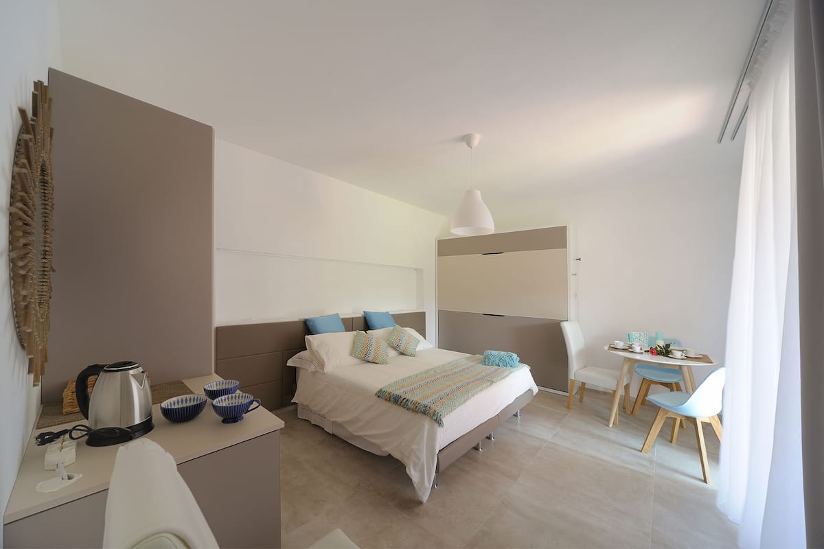 Una habitación de hotel moderna con cama, mesita de noche y un pequeño comedor.