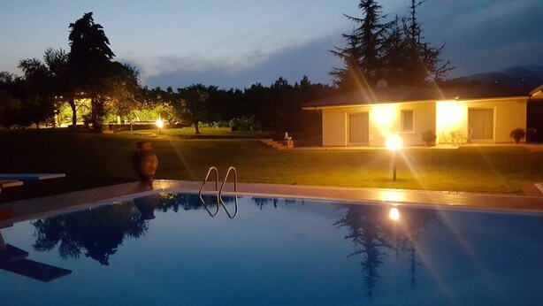 Une piscine offrant une vue dégagée sur les environs, notamment sur une maison dont les fenêtres sont illuminées et sur une pelouse bien entretenue.