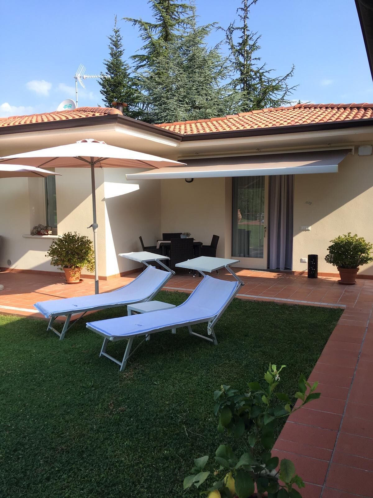 A patio with two lounge chairs, a table, and a covered area with a white umbrella.