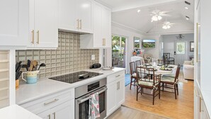 Una cocina moderna con armarios blancos, una estufa integrada y una zona de comedor con sillas de madera.