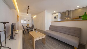 A modern living room with a sofa, a dining table, and chairs. There is a TV on a stand, a ceiling light fixture, and a kitchen area with a microwave. - B38 - Tamar 2 Bedroom Apartment in Lagos (Lagos)