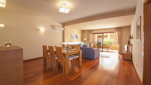 Amplia sala de estar con una mesa de comedor dispuesta para cuatro personas, un sofá y un balcón con vistas.