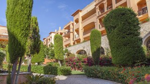 Un patio con un sendero adoquinado, setos cuidados y un edificio con balcones y ventanas arqueadas.