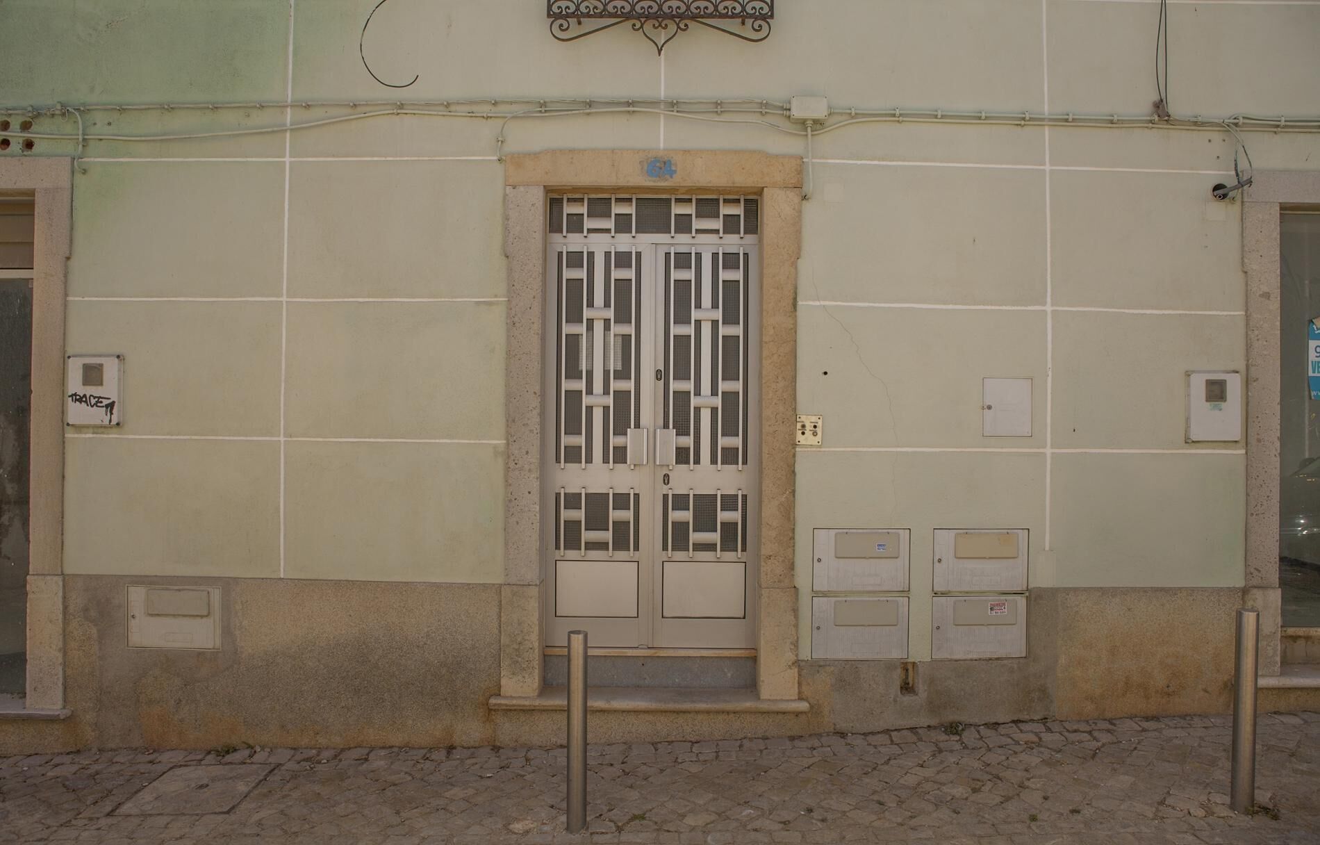 A building facade with a tiled entrance, a metal door with a grid pattern, and several electrical boxes on the wall.