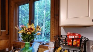 Una encimera de cocina con un florero de flores, un cuenco de aperitivos y una cesta de frutas.