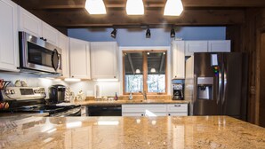 Una cocina con encimeras de granito, electrodomésticos de acero inoxidable, armarios blancos y un ventanal con vistas a árboles.