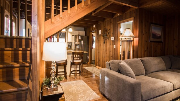 Un interior de madera con una escalera, un sofá, una mesa de comedor con sillas y una zona de cocina.