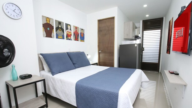 A modern bedroom with a bed, a side table, a wall clock, and superhero-themed artwork. - Studio Apartments E3 (Medellín)