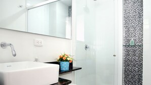 A modern bathroom with a white sink, a toilet, and a glass shower enclosure. - Studio Apartments E3 (Medellín)