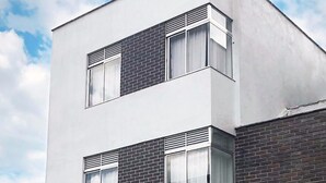 A modern two-story building with a flat roof, large windows, and a garage with a black shutter. - Studio Apartments E3 (Medellín)