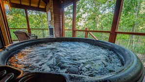 A hot tub with a control panel, surrounded by a wooden deck and a brick wall, with a view of trees in the background.