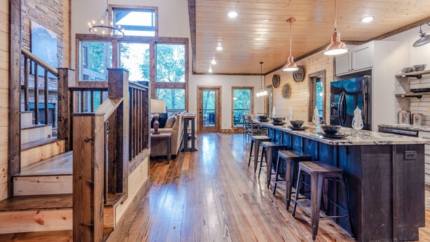 A spacious kitchen with a large island, wooden flooring, and a rustic ceiling.