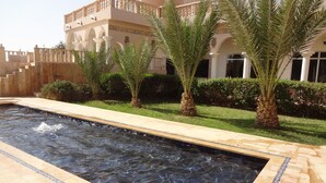 A swimming pool with a tiled edge, surrounded by palm trees and a building with a balcony.