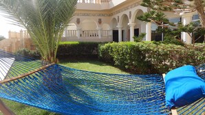 A hammock with a blue cushion in a courtyard with a building in the background.
