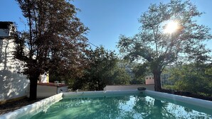 Une piscine bordée de blanc, entourée d’arbres et de bâtiments.
