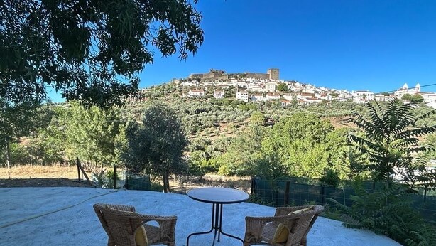 Un espace extérieur aménagé avec des chaises et une table en osier, offrant une vue sur une colline où se trouvent des bâtiments et une structure ressemblant à un château.
