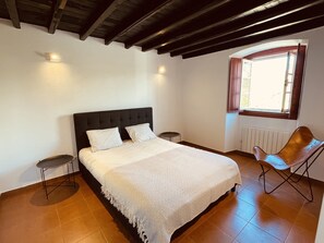 Een slaapkamer met een bed, een stoel, een nachtkastje en een raam.