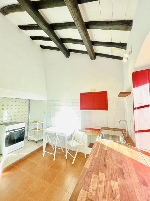 A kitchen with a wooden ceiling, white cabinets, a red cabinet, a white table with chairs, a wooden countertop, and a stove.