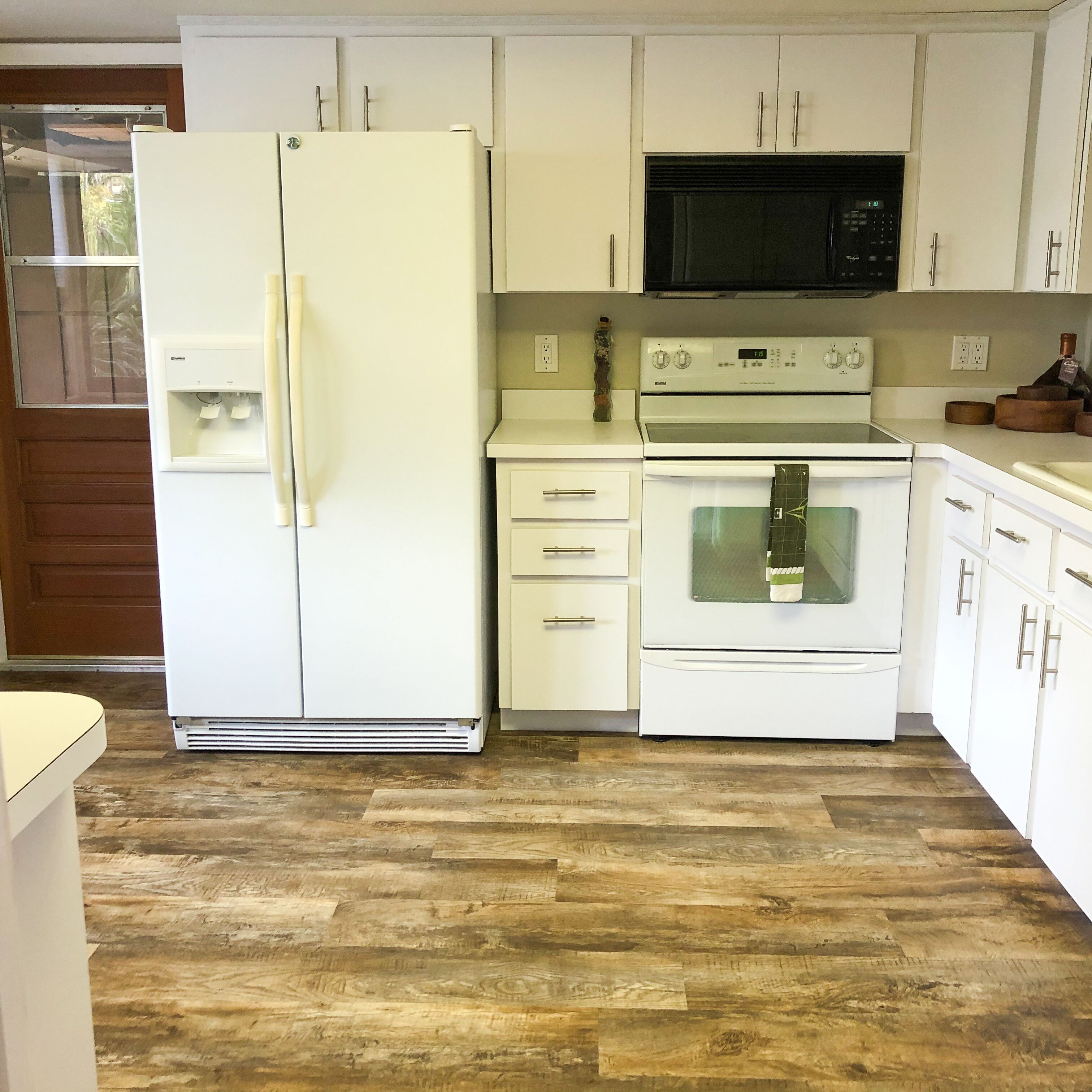 A kitchen with white cabinets, a refrigerator, a microwave, an oven, and a water dispenser.