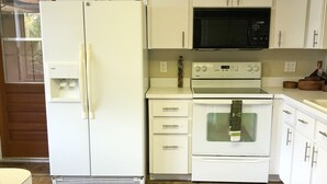 A kitchen with white cabinets, a refrigerator, a microwave, an oven, and a water dispenser. - River House - Overlooking the Scenic Withlacoochee River - Sleeps 4. (Inglis)