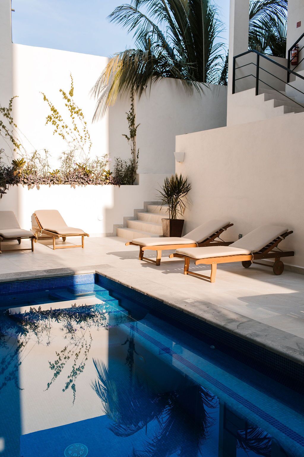 Un área de piscina moderna al aire libre con sillones de descanso y una escalera.