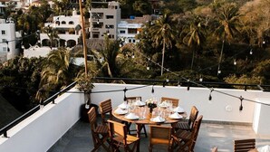 A rooftop dining area with round tables set for six, surrounded by wooden chairs.