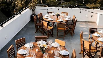 Un área de comedor en la azotea con mesas redondas dispuestas para seis personas, rodeada de sillas de madera.
