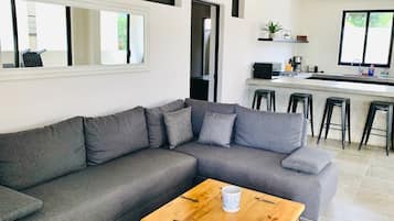Una sala de estar moderna con un sofá seccional gris, una mesa de centro de madera y una zona de cocina con barra y taburetes.