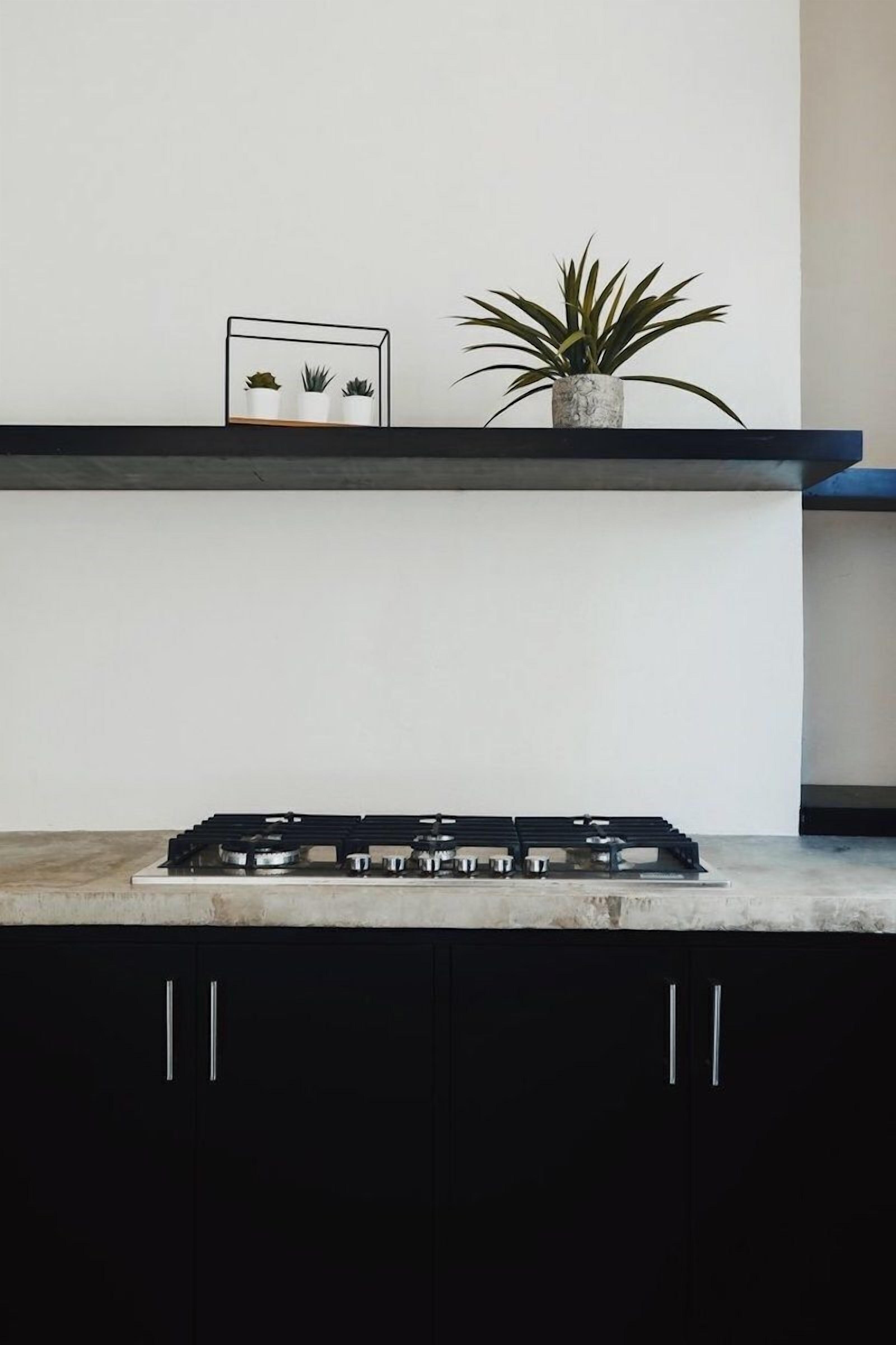 Cuina amb fogó a gas, armaris negres i taulell blanc.