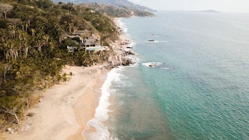 Una propiedad costera con playa, montañas al fondo y vista despejada al océano.