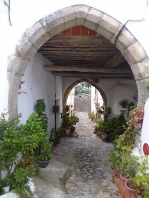 Un étroit sentier de pierre, passant sous une arche en pierre, de part et d’autre de laquelle sont disposés des pots de plantes.