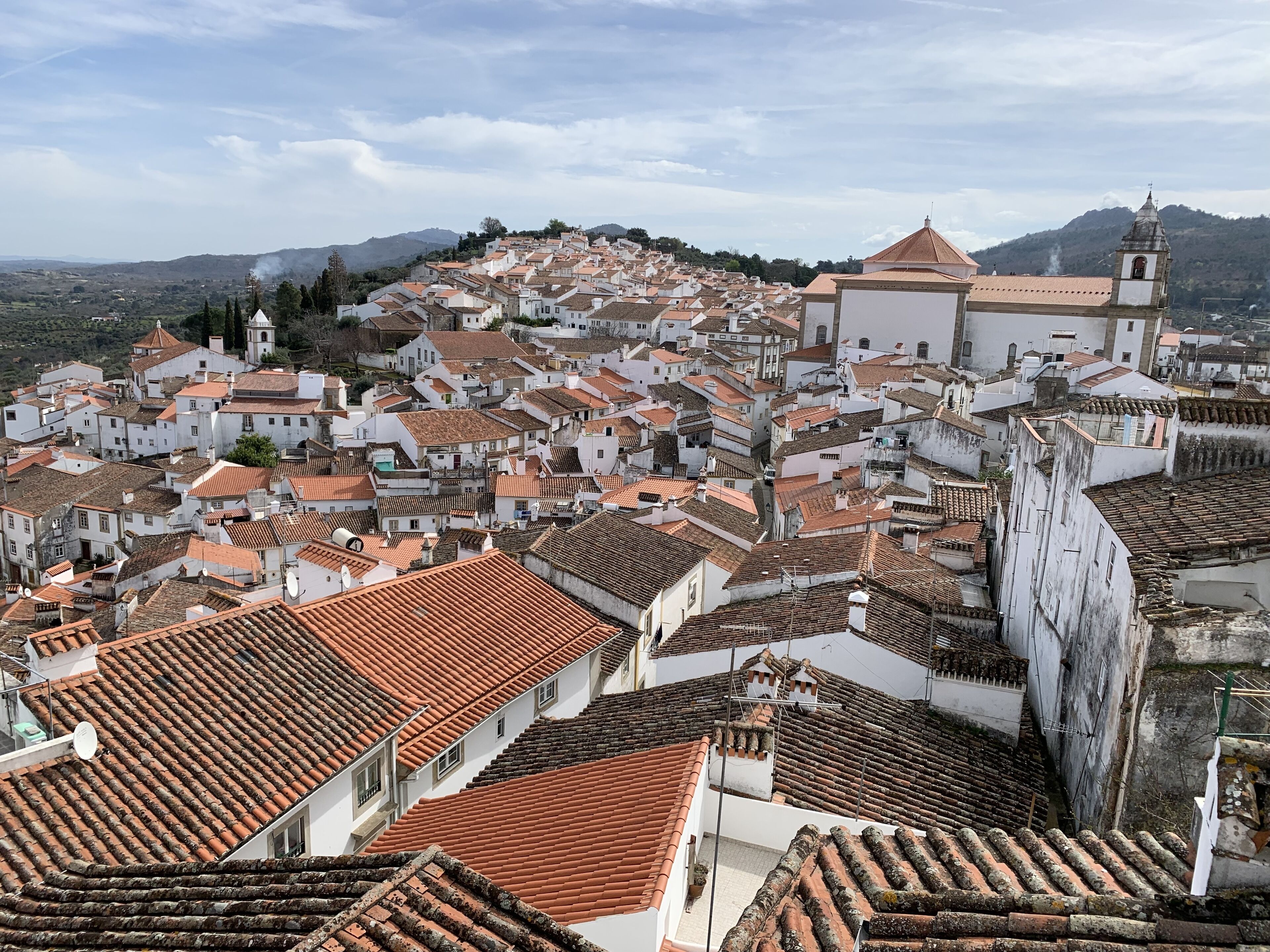 Une ville densément peuplée, avec des toits recouverts de tuiles en terre cuite et des bâtiments blancs, dont une église dotée d’un clocher.